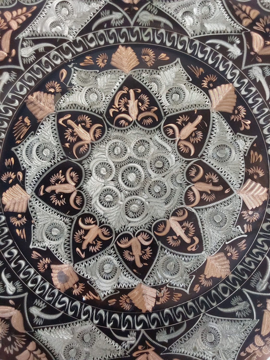 Close-up of the centre of the plate, showing fine etched rings and petal shapes in silver and copper, with some light wear on the copper areas.