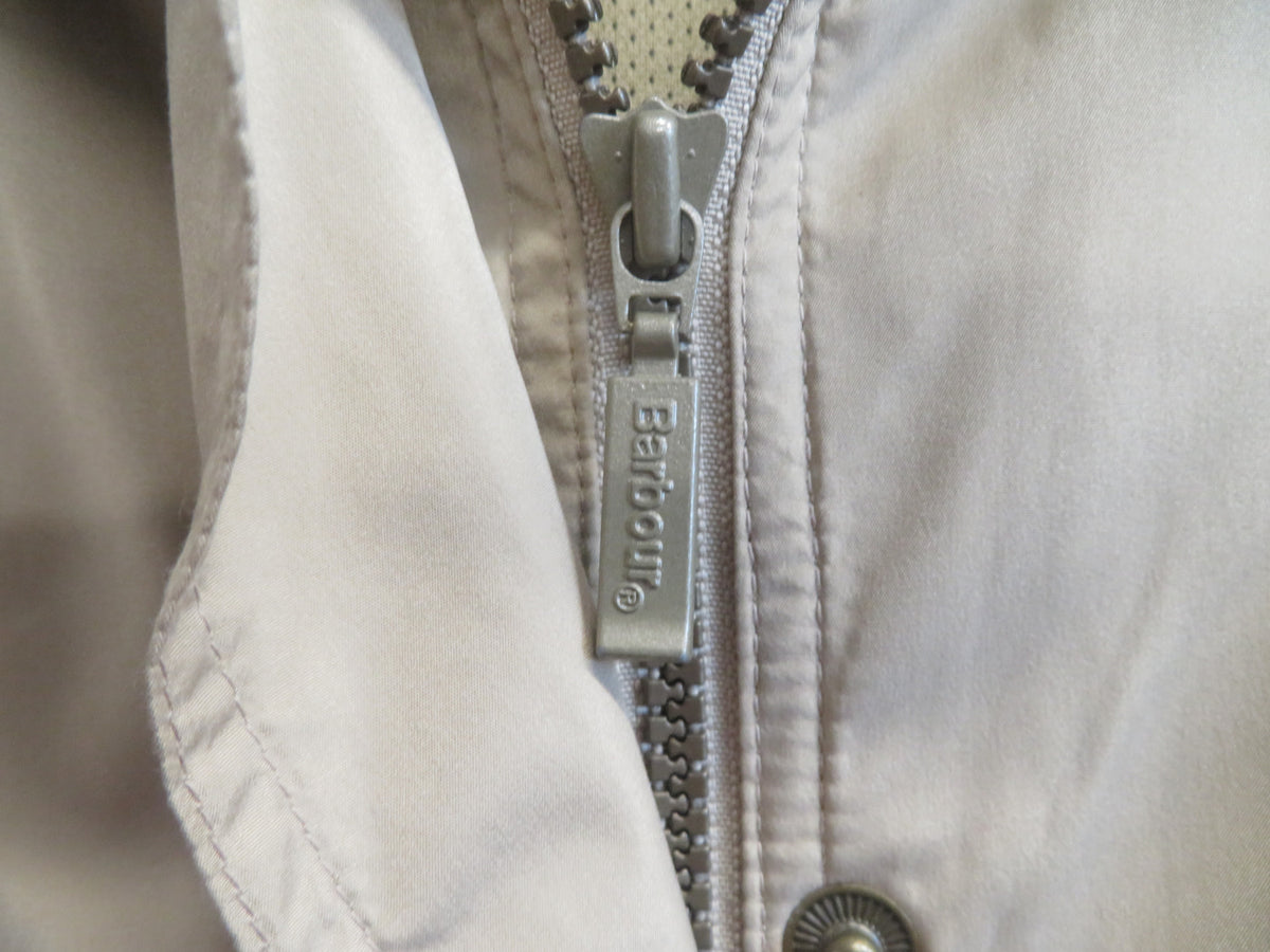 Close-up of the front zip with a metal pull tab marked Barbour, beside a snap fastener.